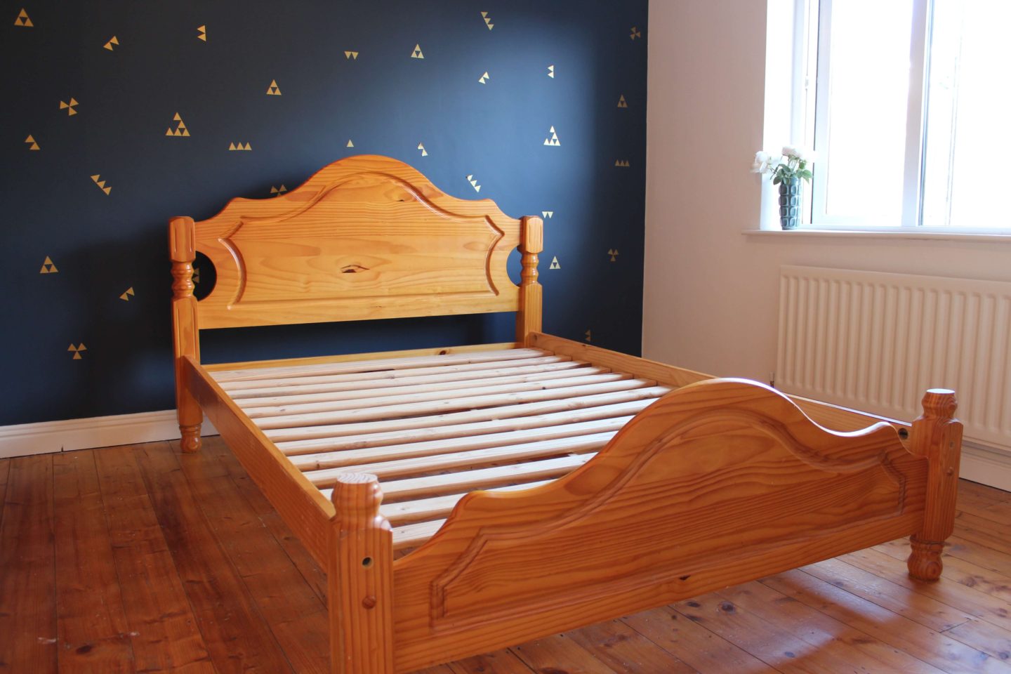 A guestroom with navy wall, gold decals and a pine bed.