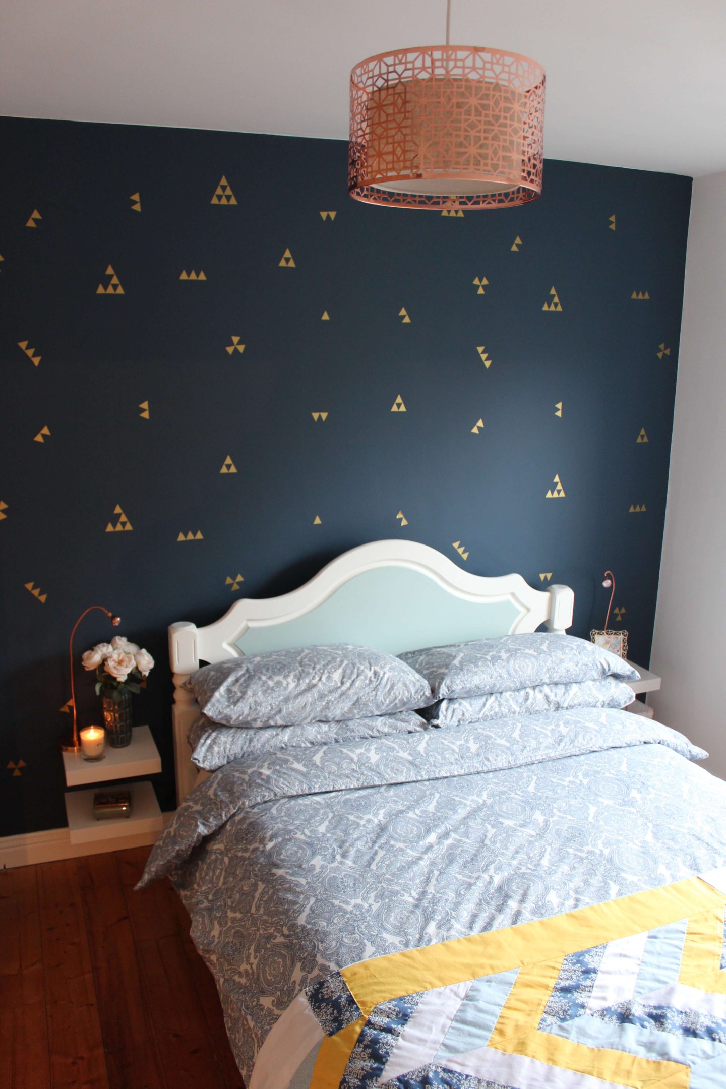 A reveal guestroom photo of a painted white and duckegg bed, set against a navy wall with gold decals.