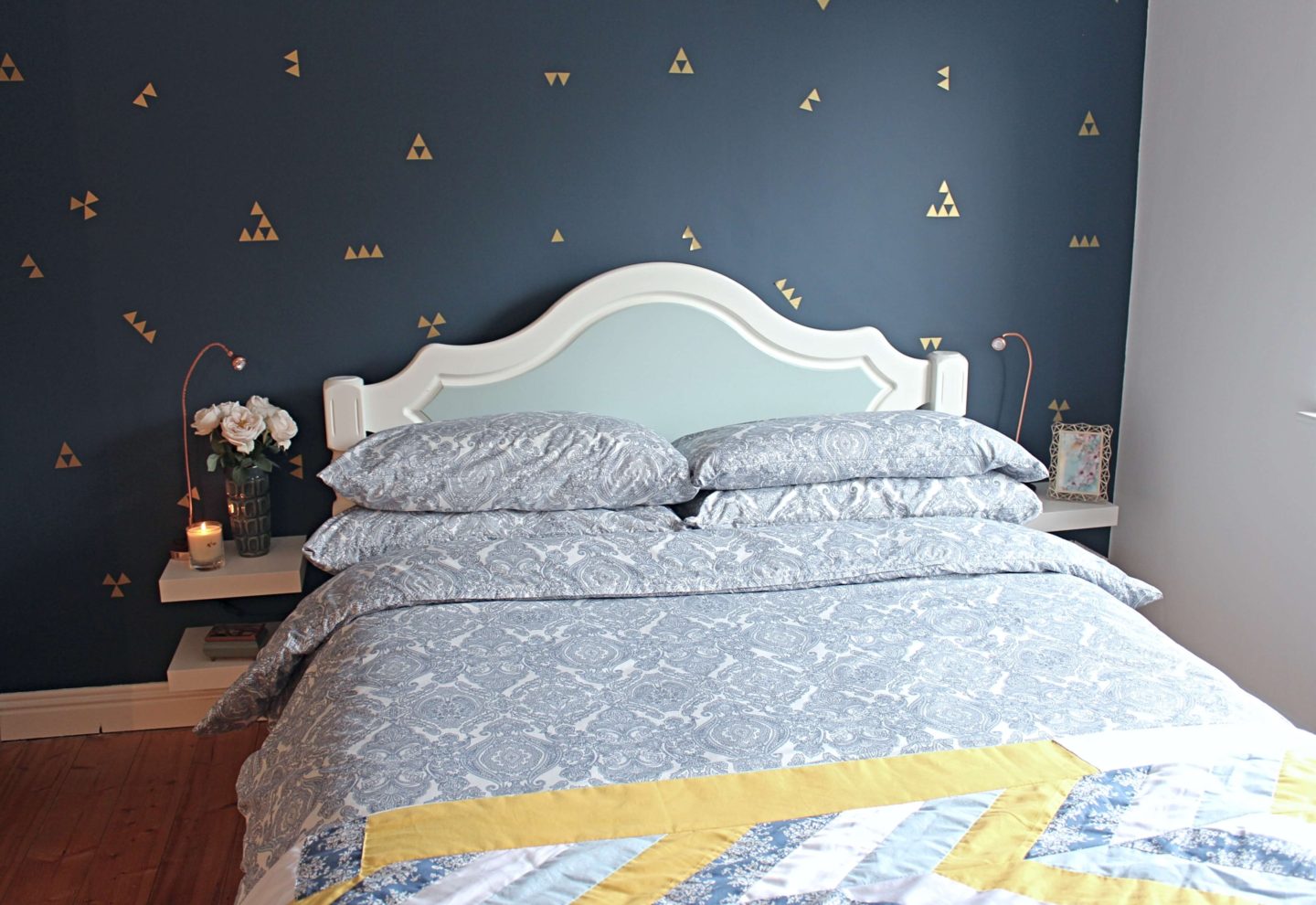 Bedroom with navy feature wall with gold triangular decals. 