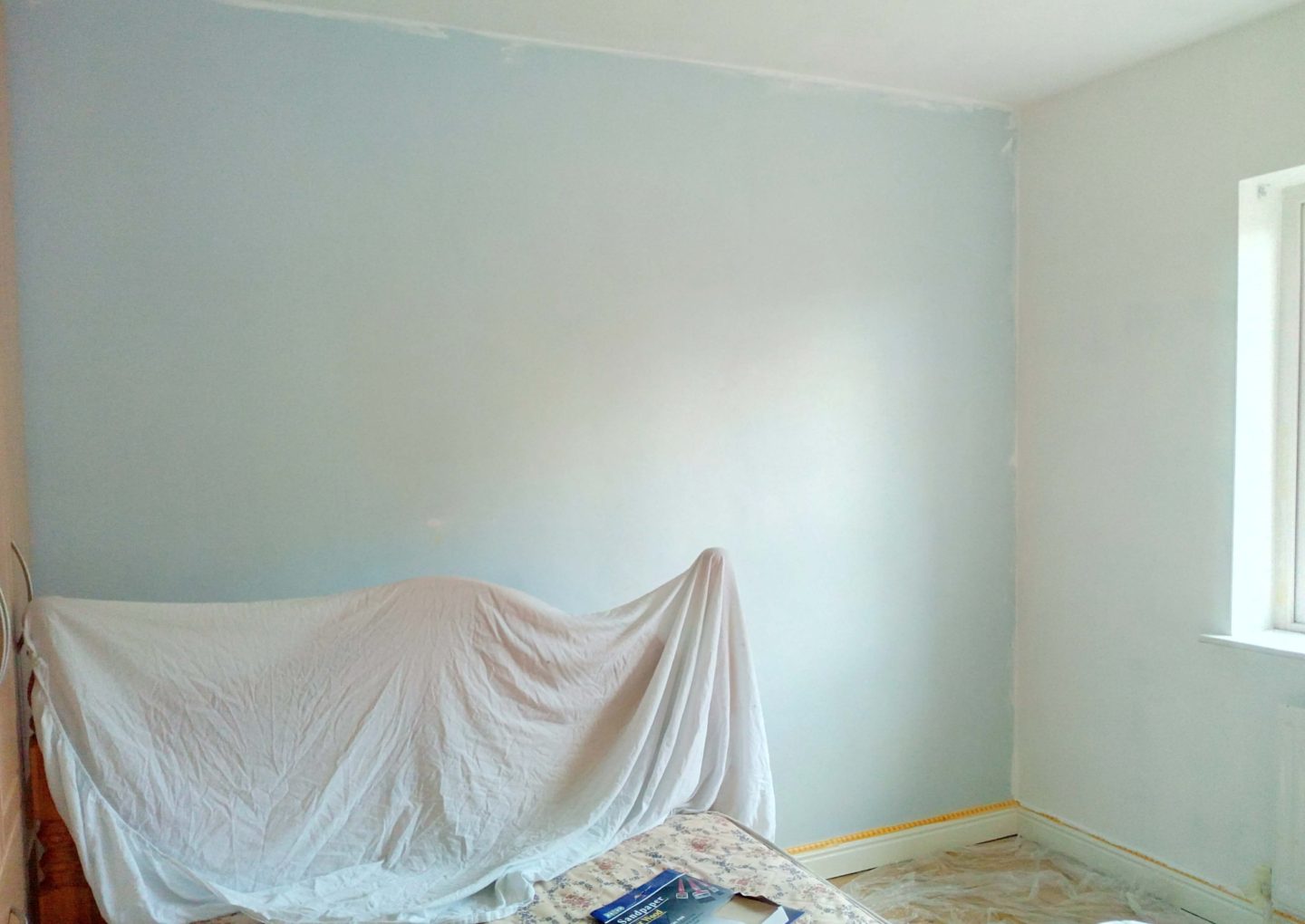 A before photo of an empty guestroom with pale blue walls.