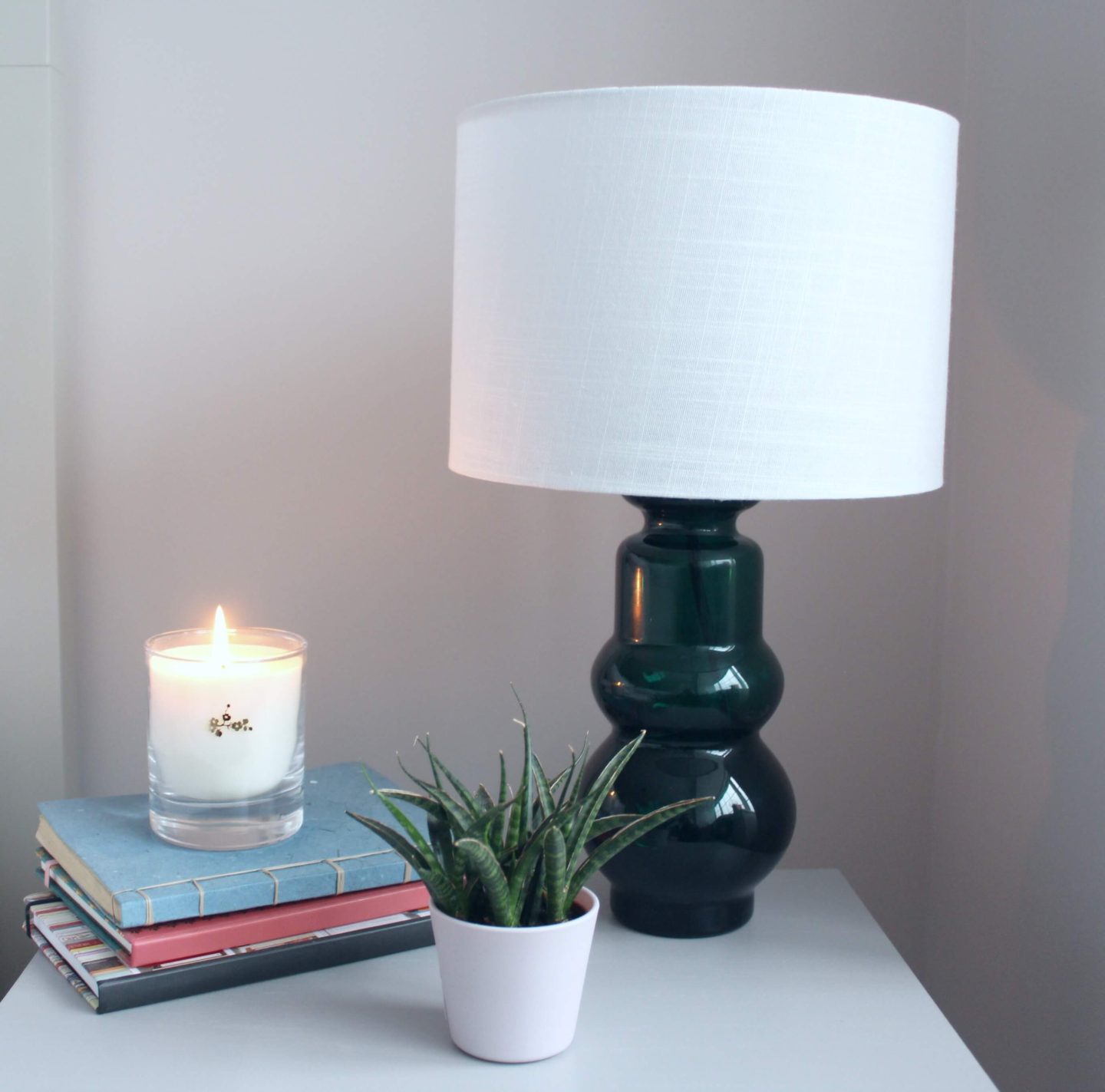 A green glass lamp with a white drum lampshade. 