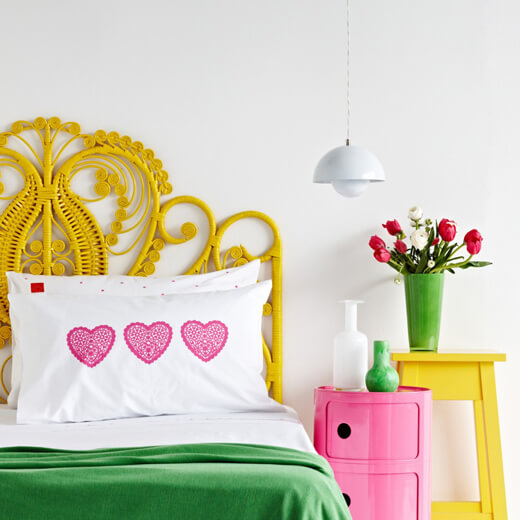 bedroom white walls, yellow boho headboard, white and green duvet, colourful bedside tables