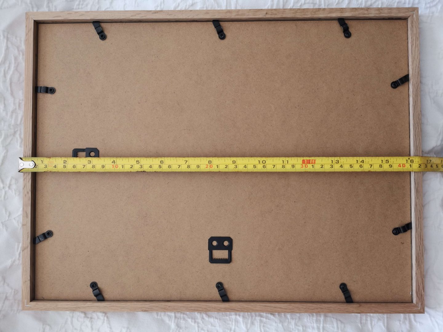 A measuring tape showing the distance between the top of a picture frame and it's hanging hardware.
