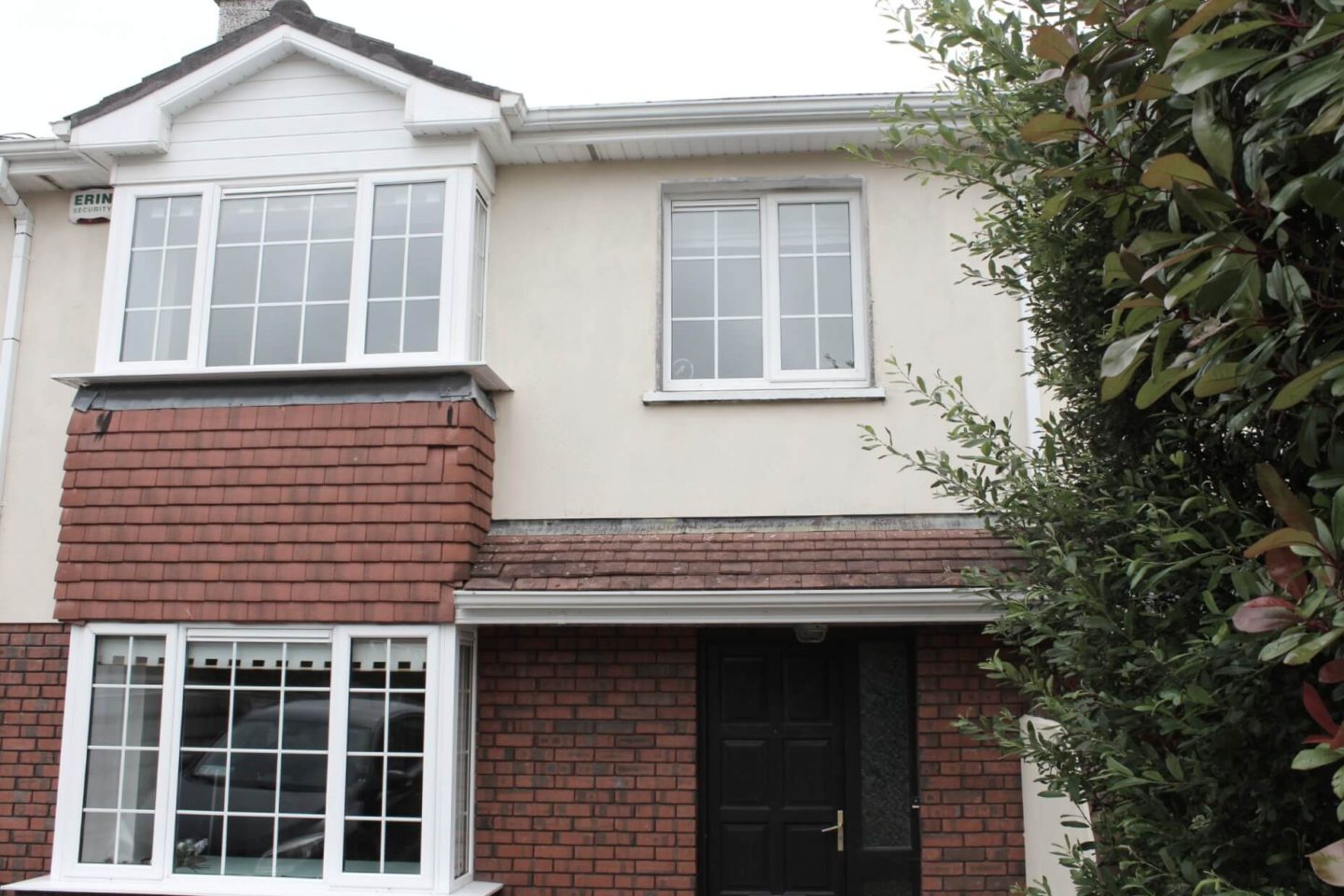 The beginning of a house tour of a semi detached house. Red brick on lower half and magnolia paint on top. Black front door.