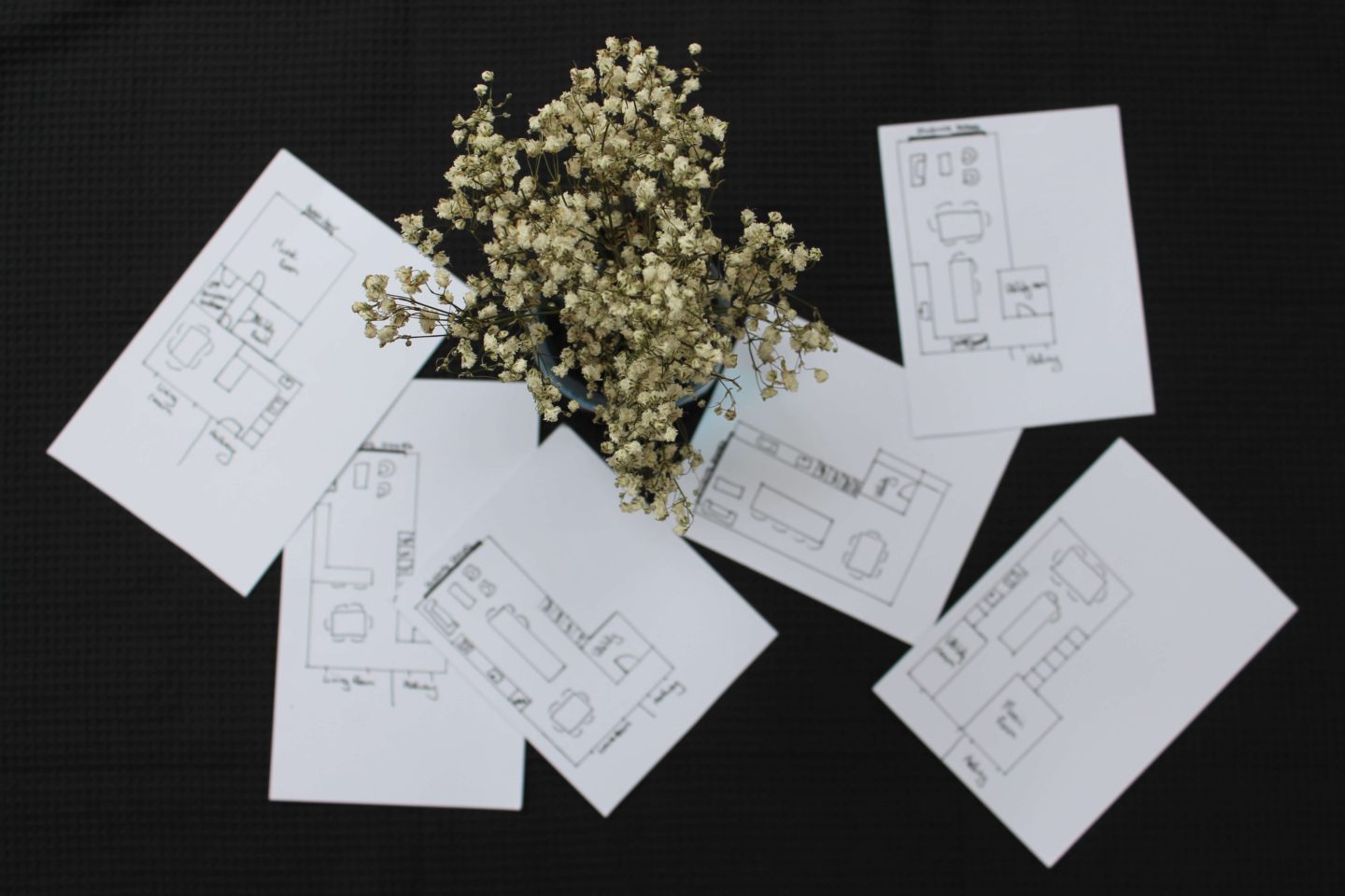 Paper cards with lots of kitchen layouts drawn. Vase of white flowers.