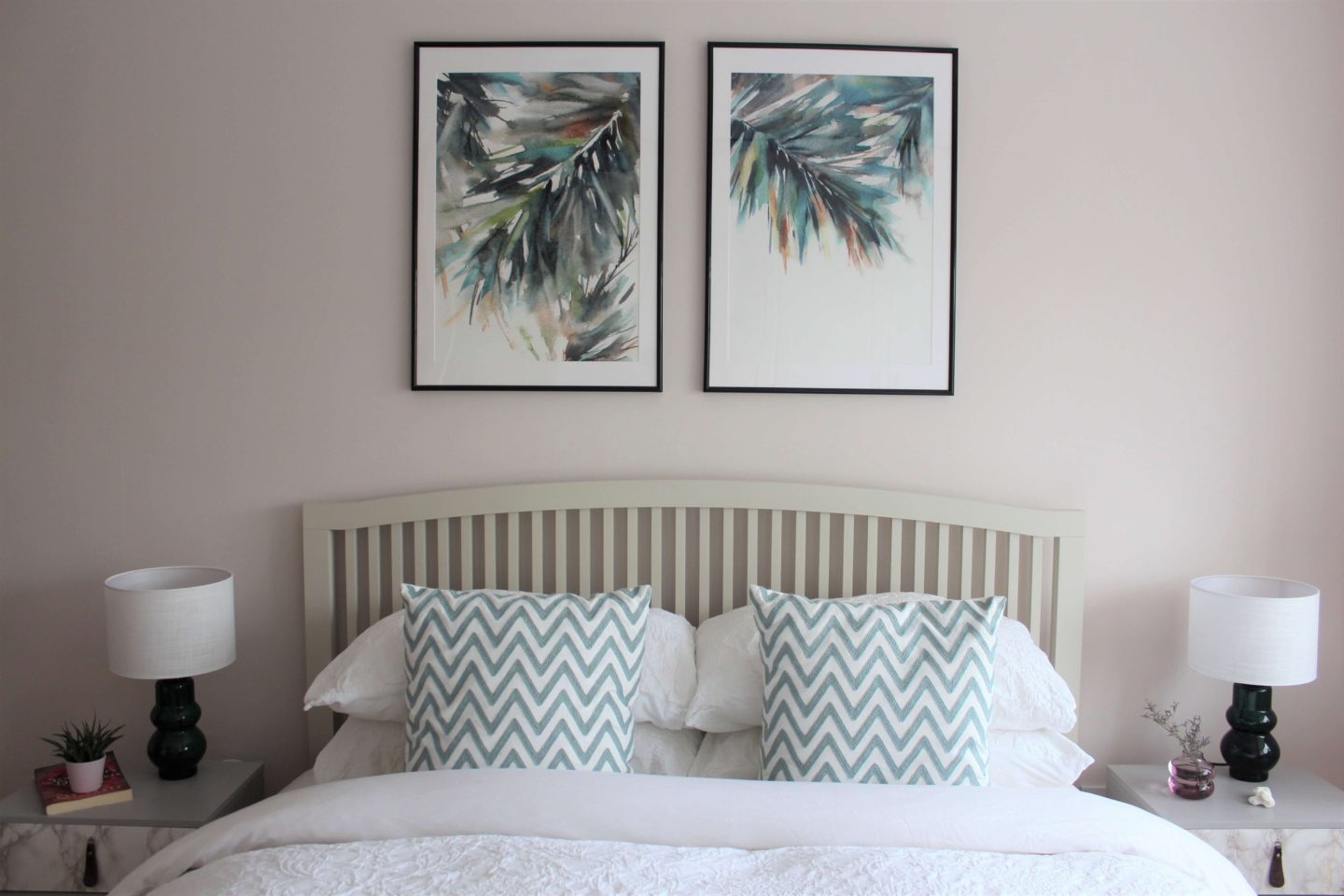 Bedrrom with pink wall, palm leaves artwork and white bed linen.