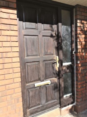 Brown stained front door lightly sanded. Masking tape in areas prepped for painting.