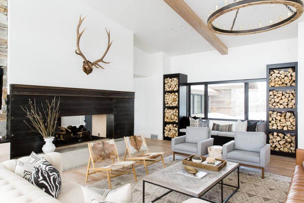 Modern cabin living room with a large fireplace, logs piles, a grey coffee table with seating all around.