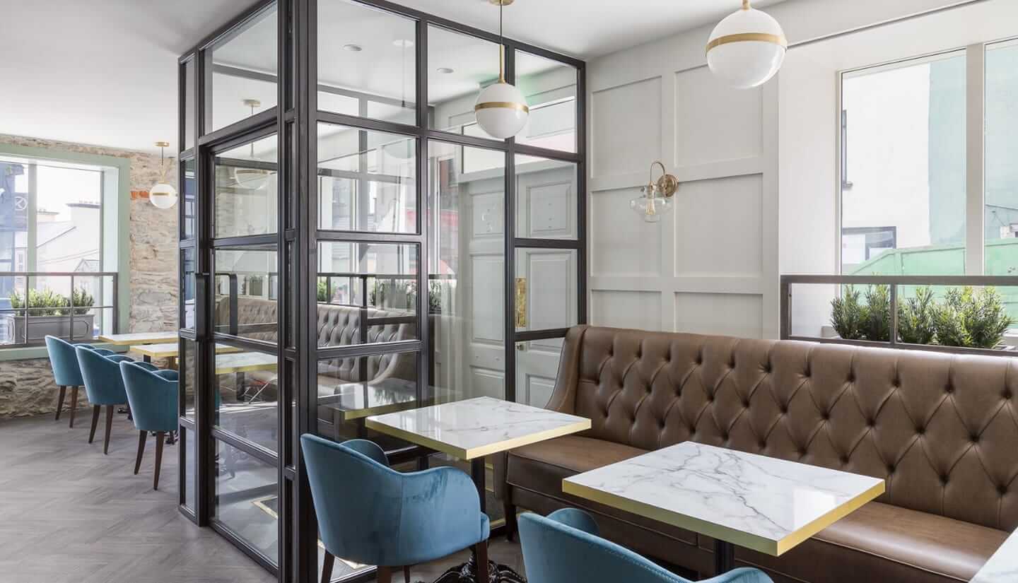 A restaurant with dark leather benches and blue velvet chairs. Tables have marble tops.