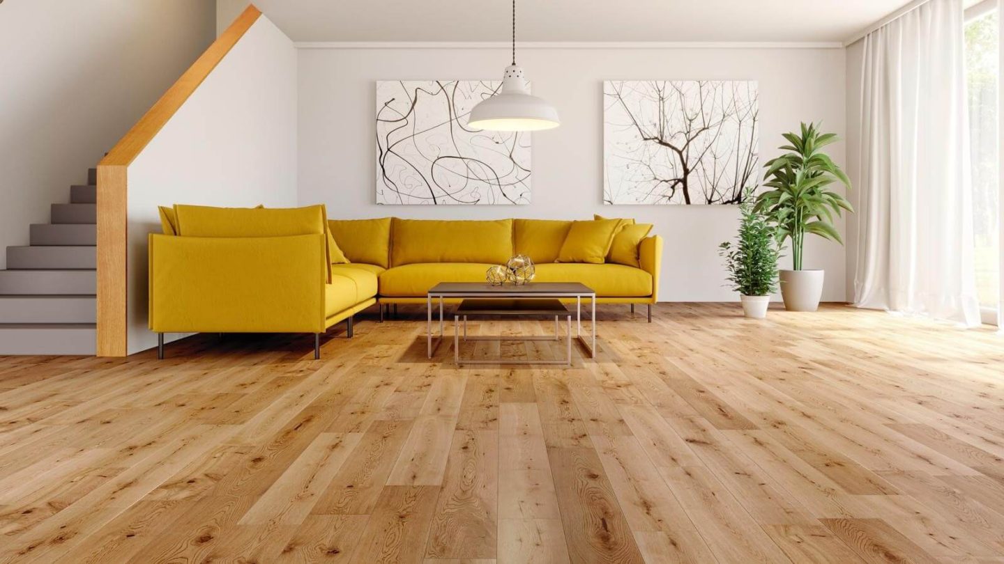 A living room with a yellow couch and two large plants. Floors are medium coloured hardwood.