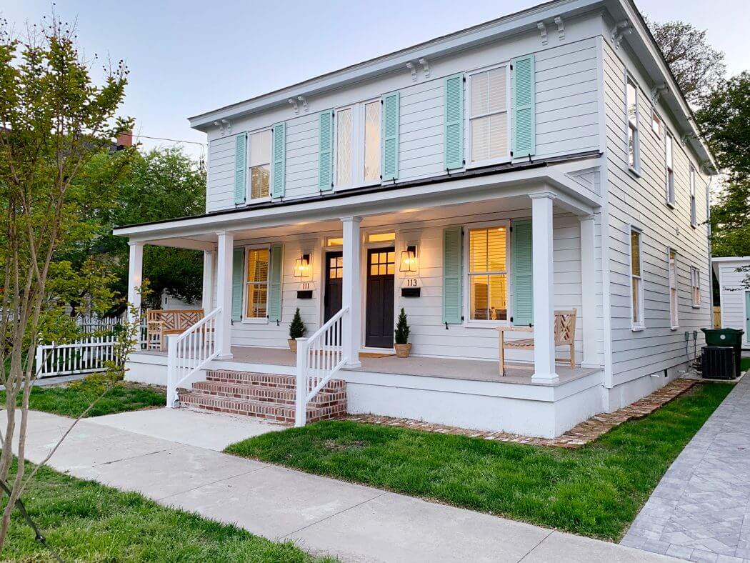 A white duplex with mint green shutters and a large porch.