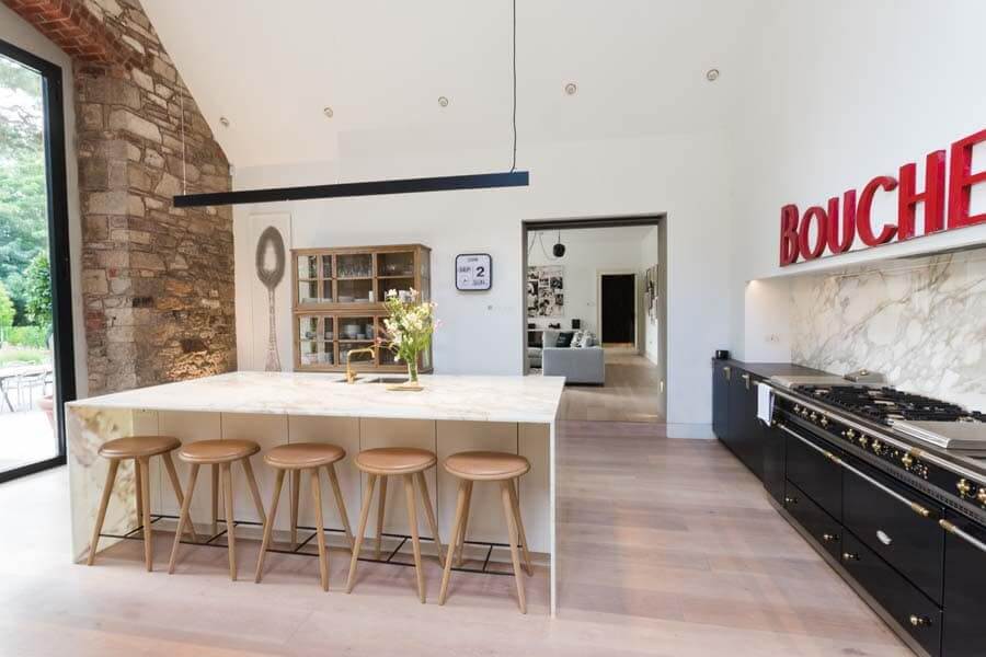 A kitchen with white walls, some exposed brick and a large marble island. 