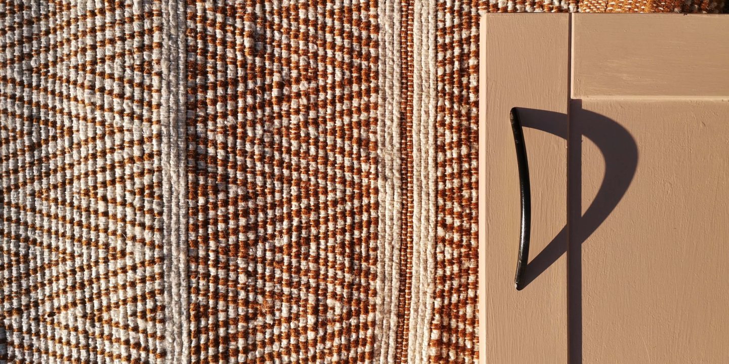 A pink cabinet door with black handle against a background of a patterned jute rug.