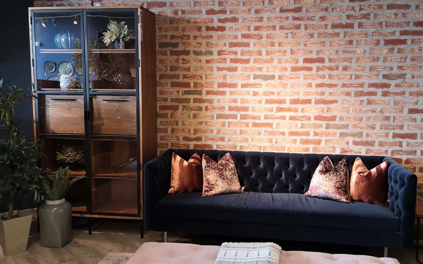 Living room with a ref brick wall, navy velet couch and a wooden dresser.
