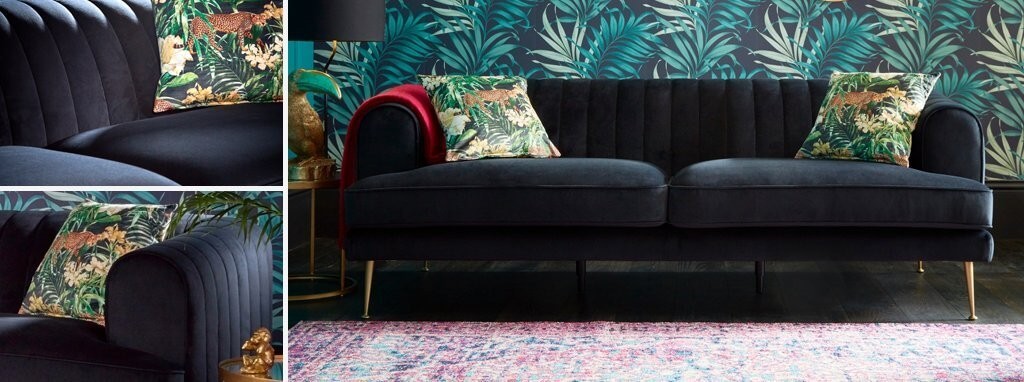 A black velvet couch against a palm tree wallpaper background.
