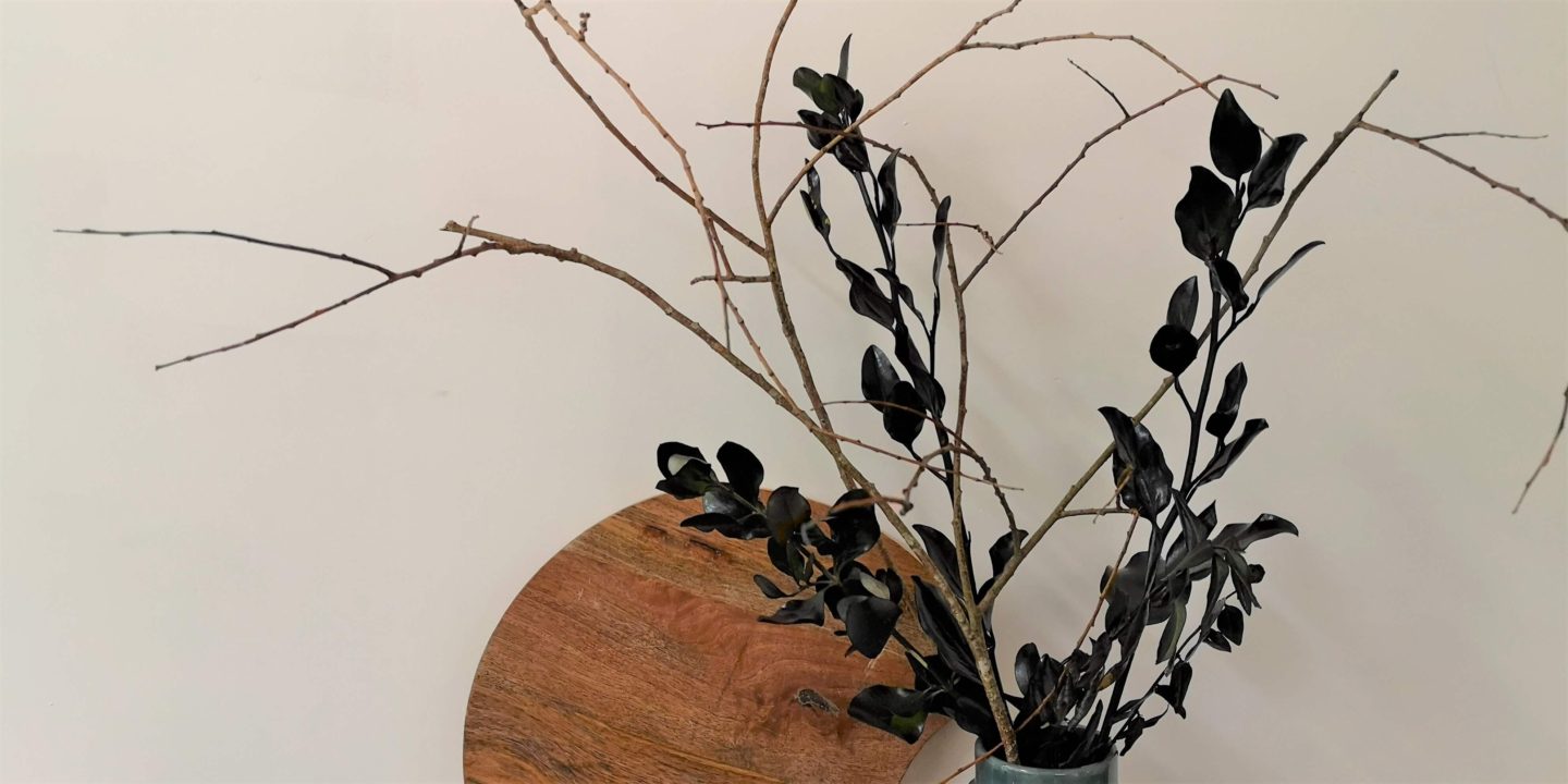 A close up of the Halloween greenery. Black spray painted greenery interspersed with bare twigs in a dark green vase. 