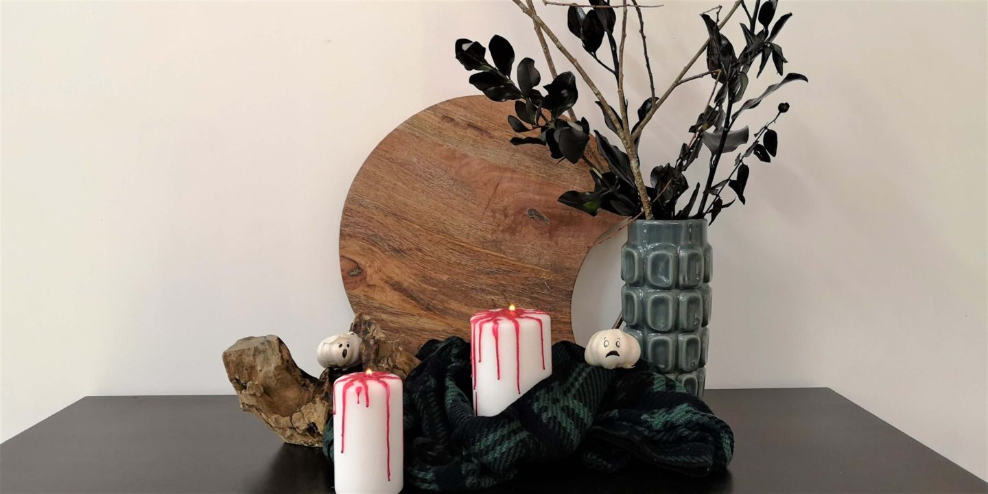 A display of Halloween decor. Black greenery, candles and garlic bulbs with ghost faces drawn on them.