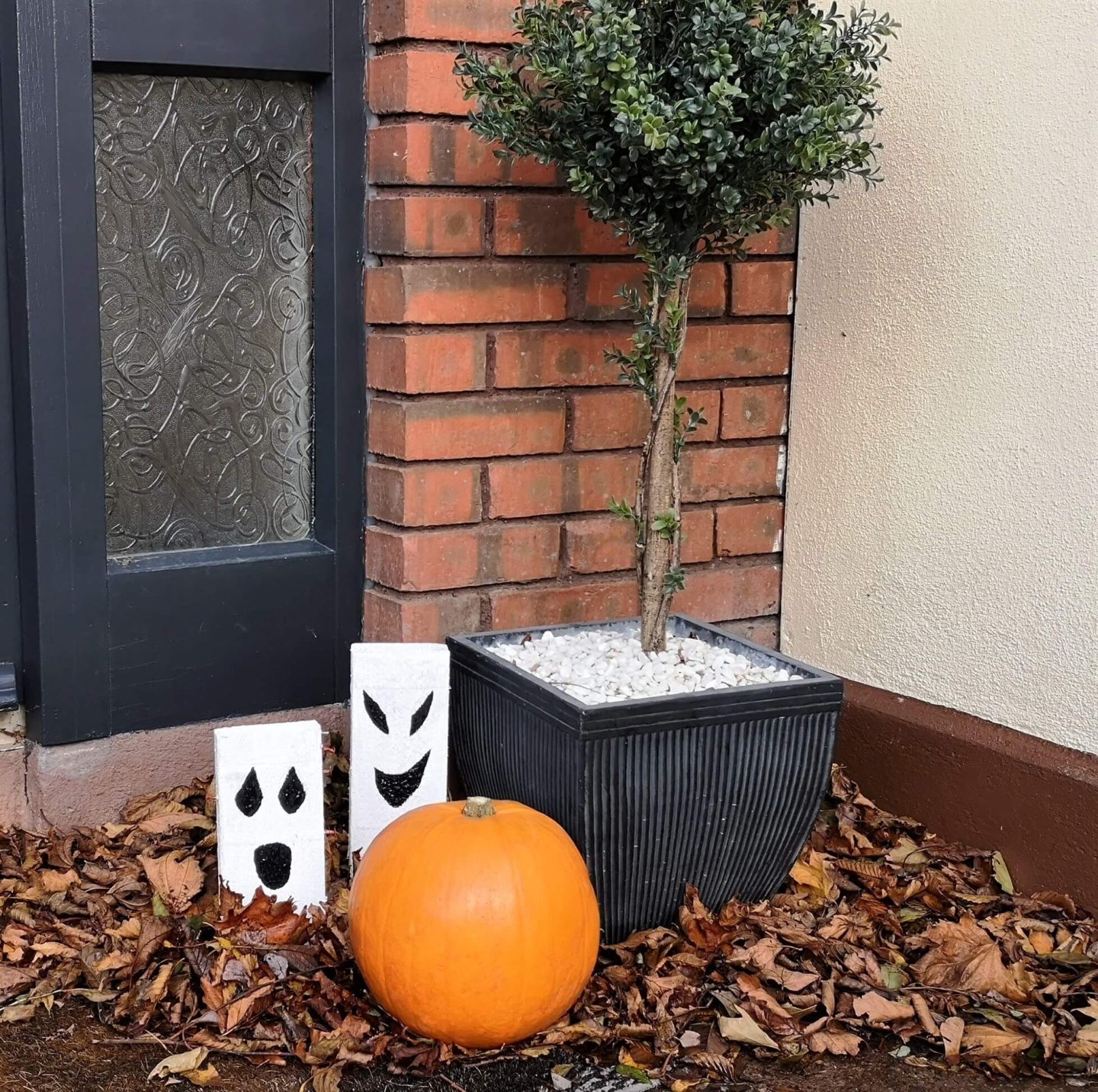 Front porch with two wooden ghost and a pumpkin next to a potted tree.