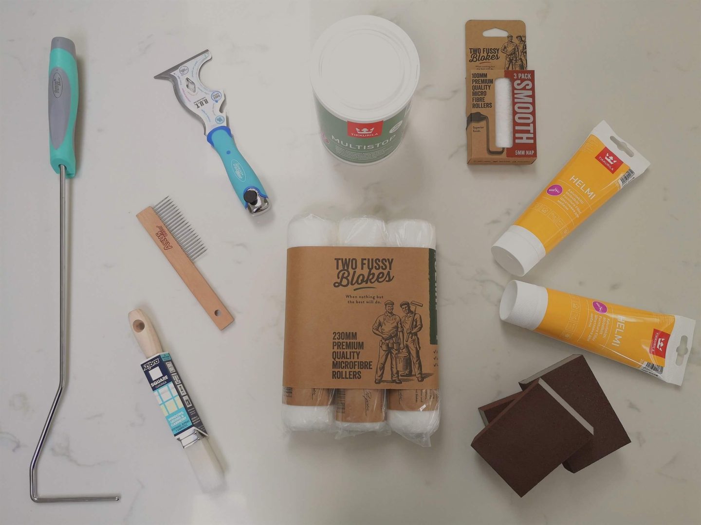 A flatlay of the most basic painting tools, inclusing a paint brush, roller, sandpaper and brish comb.