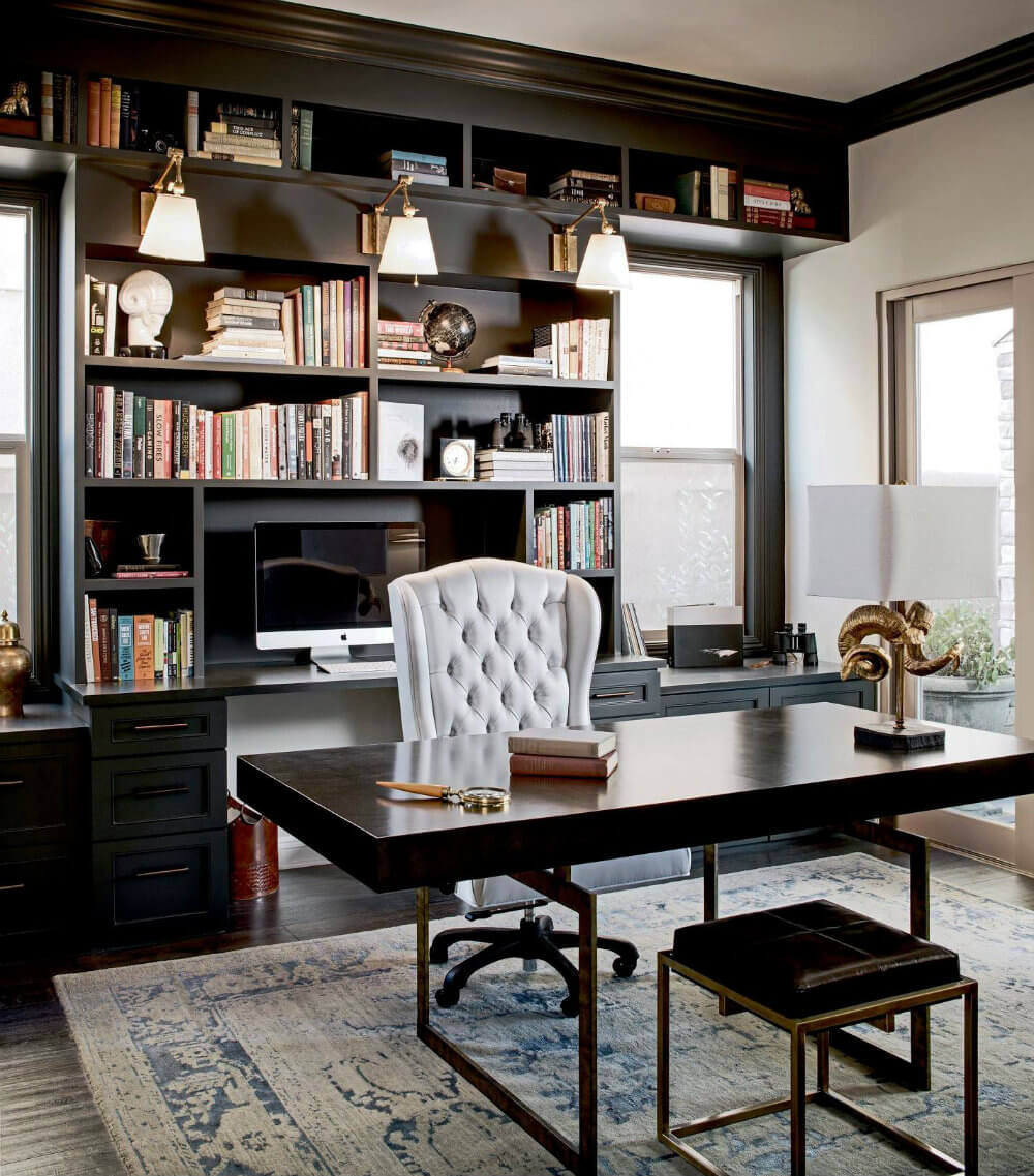 A home office with dark navy walls, shelving, a wooden desk with a white fabric chair.