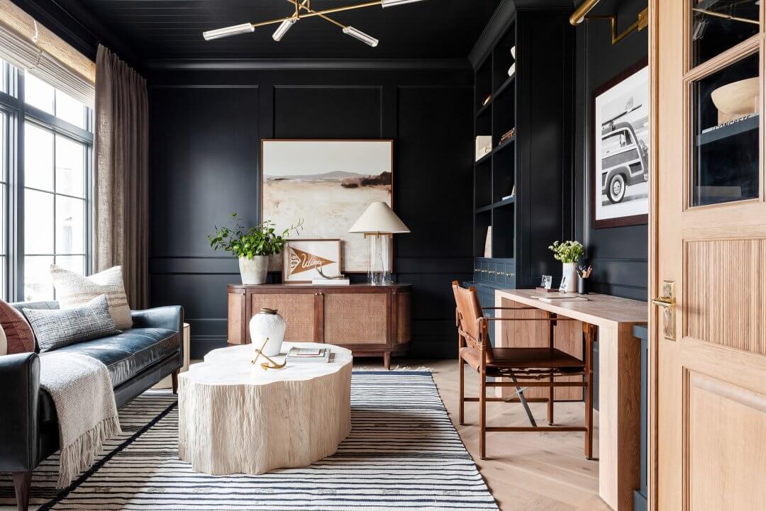 A home office with black walls and a coffee table made out of a large tree stump.