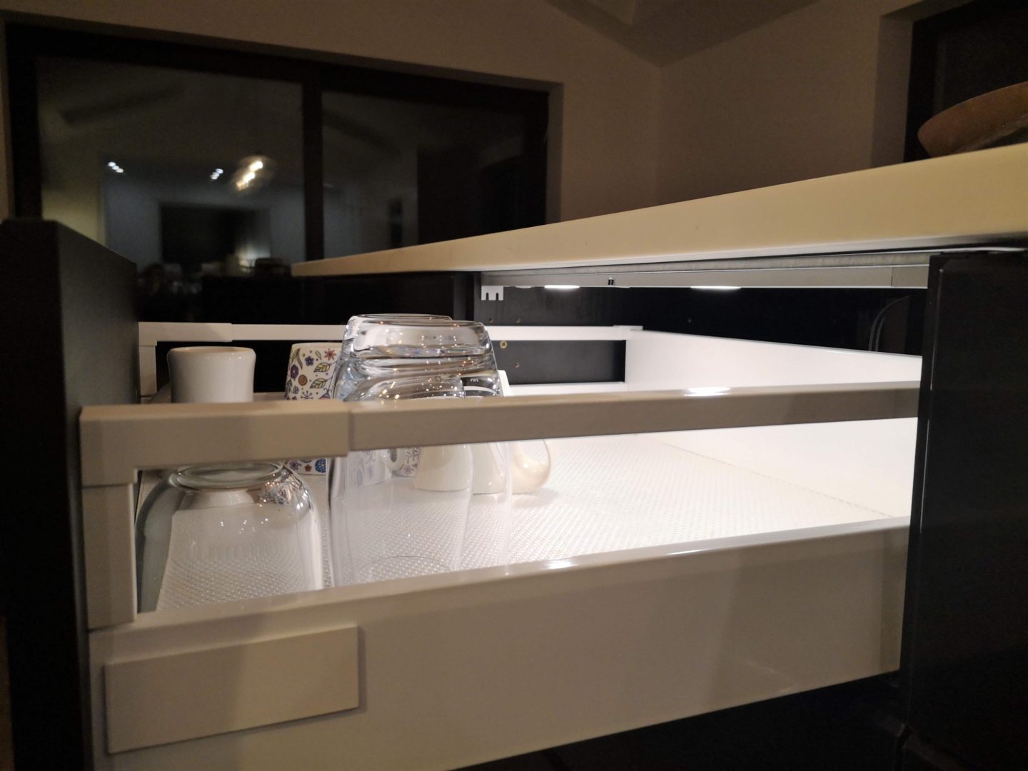 An open kitchen drawer at night with in cabinet lighting.