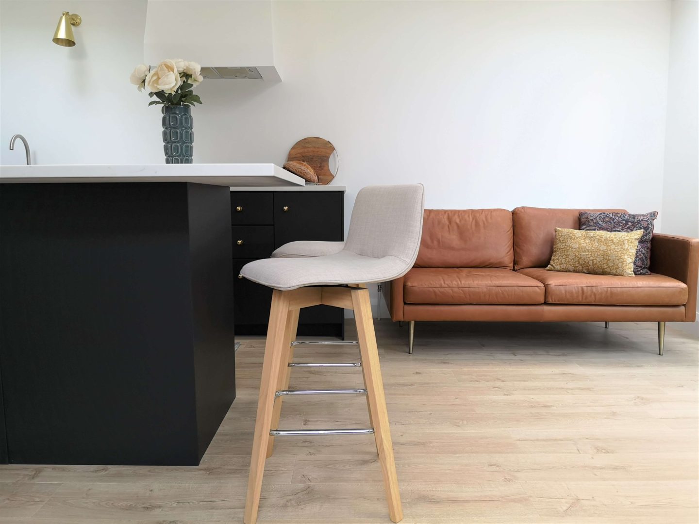 A black kitchen with white countertops and walls. Two kitchen beige stools are shown next to a leather couch.