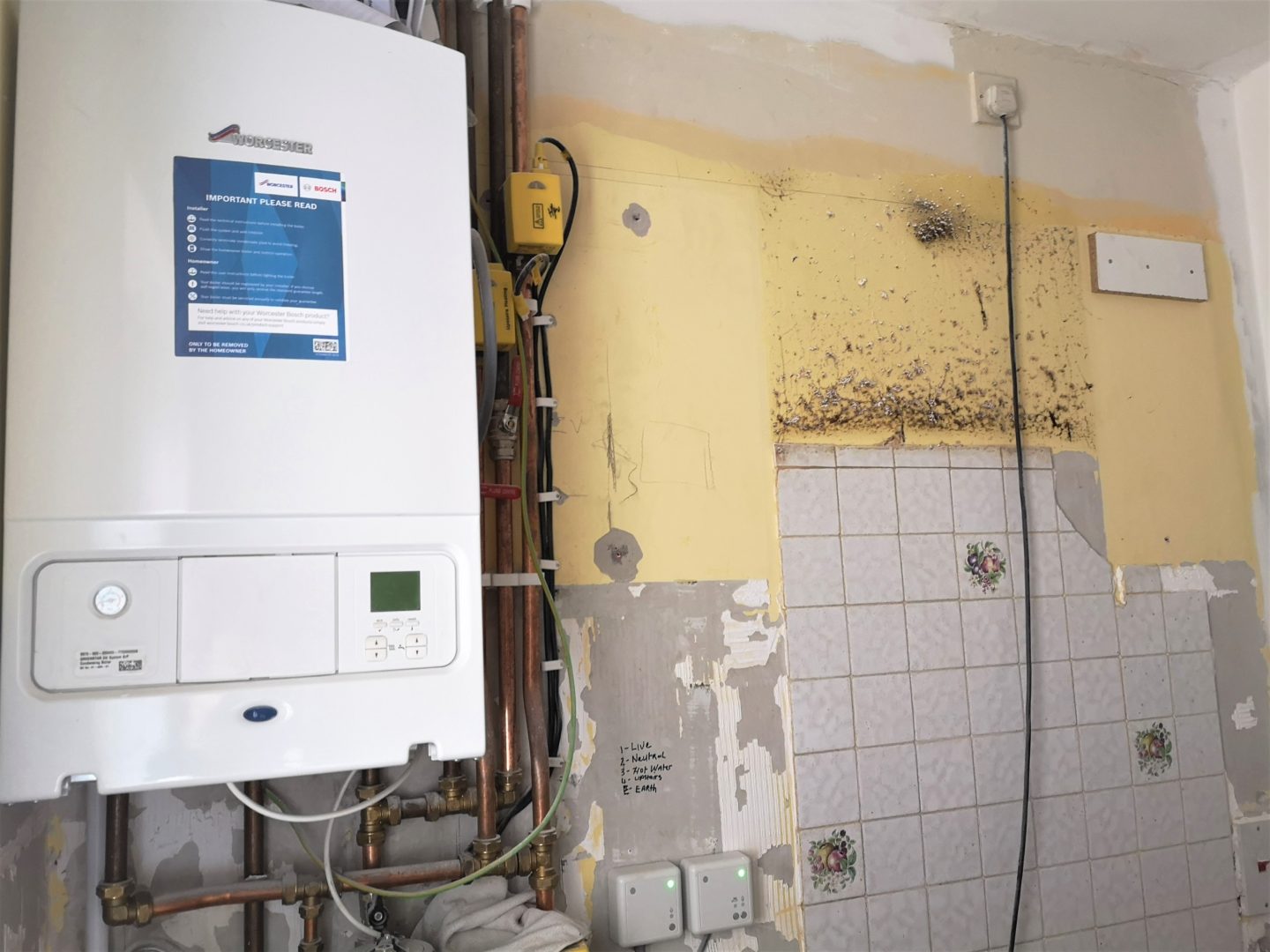 A boiler against an old wall of tiles and mould, mid renovation.