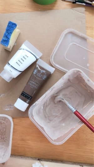 Brown and white acrylic paint mixed together in a tub to create a dark beige colour.