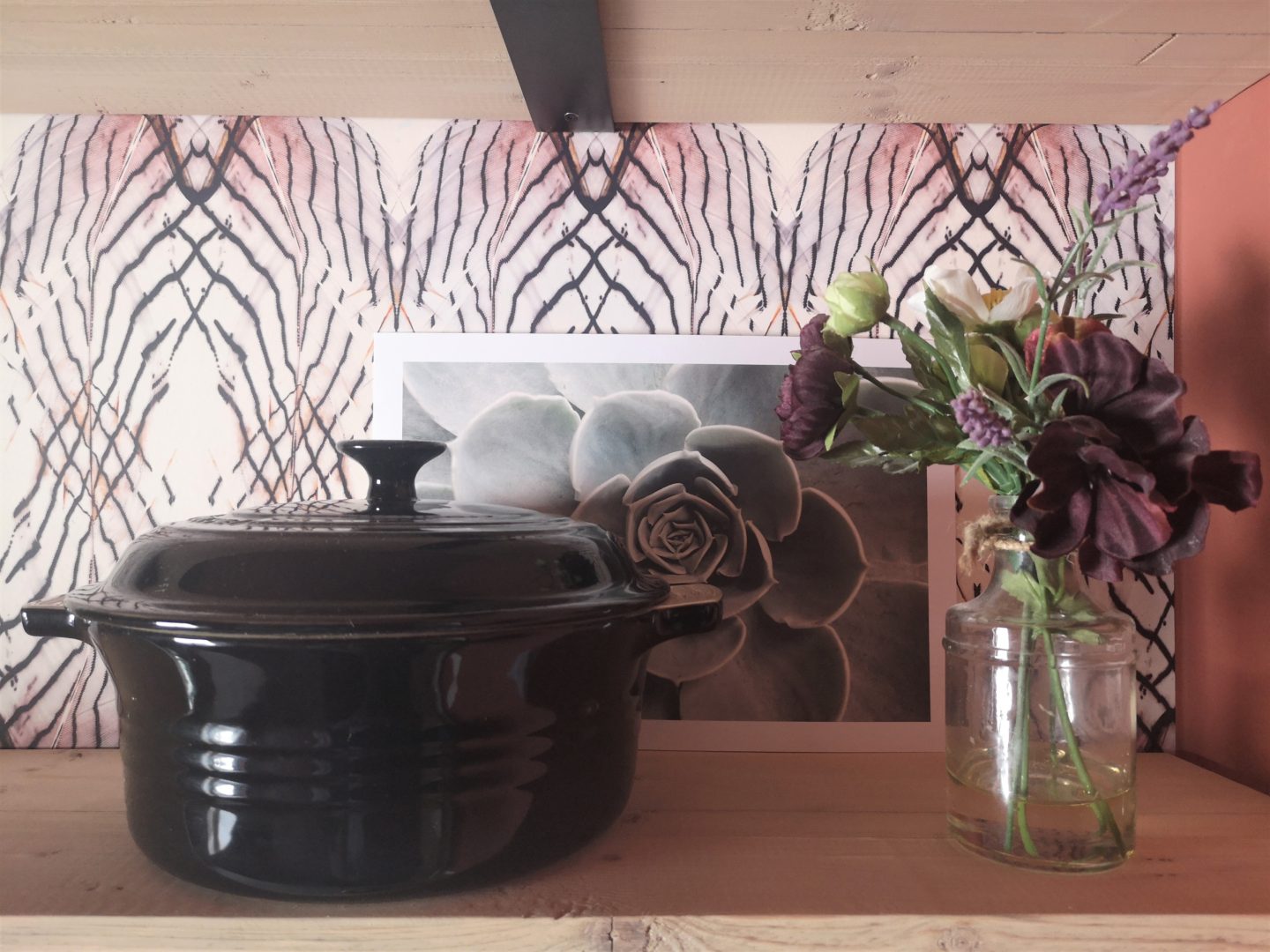 A close up of shelves, showing artwork, flowers and a black pot.