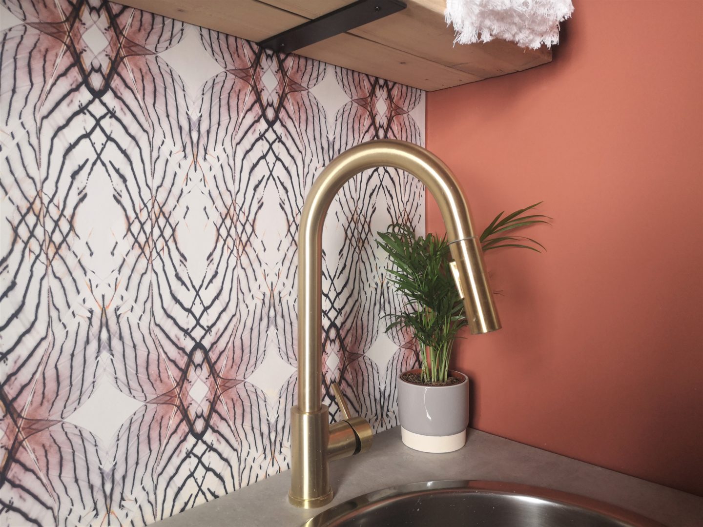 A brass utility room tap with a wallpapered wall.