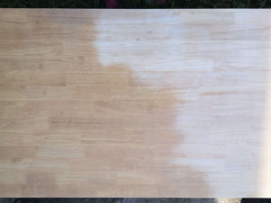 A light wood table with half of an orange looking stain sanded off.