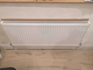 A white radiator with a thin board of MDF screwed into the wall above it.