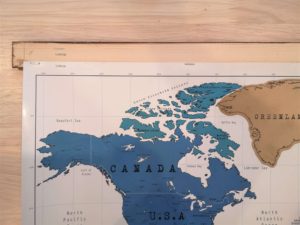 The top of a world map stapled to a pine slat.