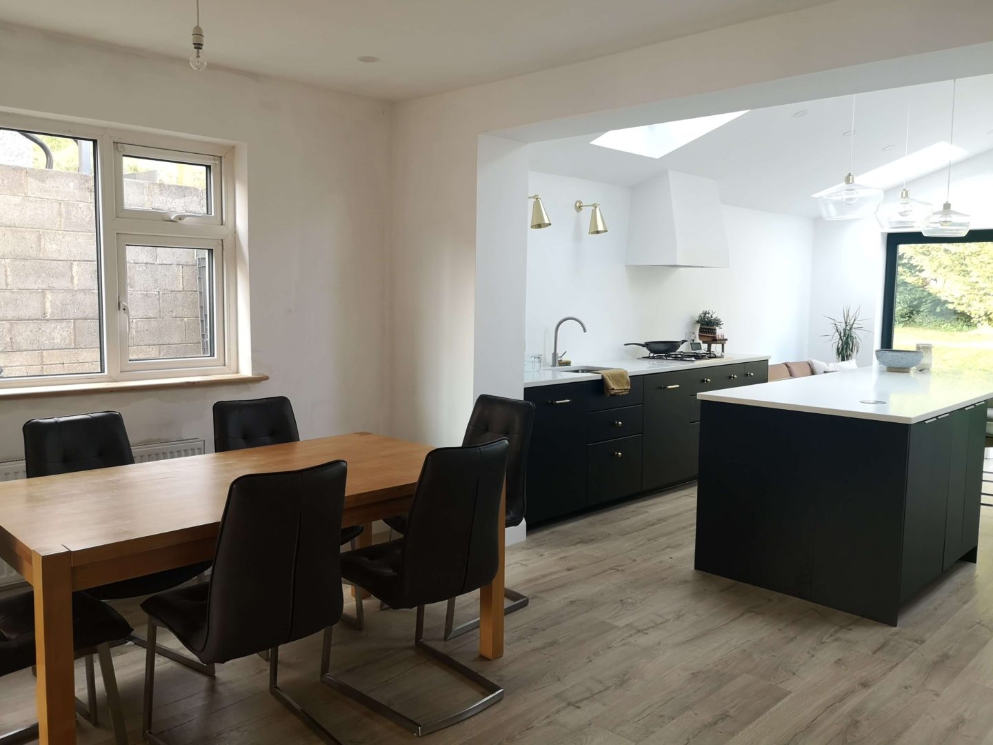 A dining area next to an open plan kitchen with black cabinets.