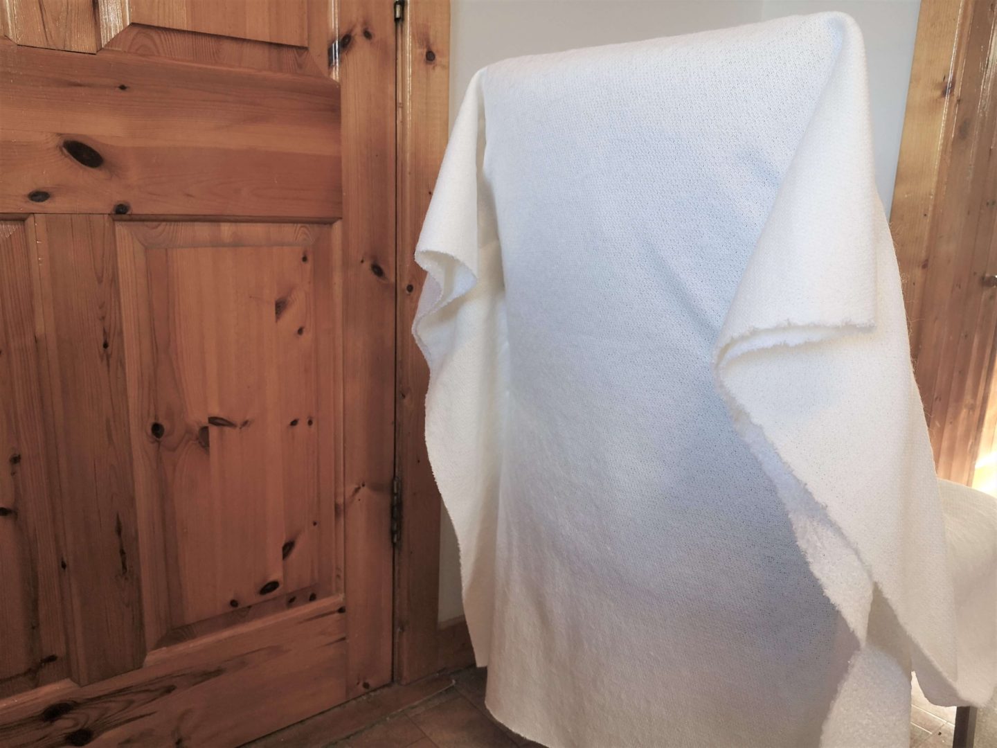 The back of a dining chair with material draped over it and held in place with pin needles.