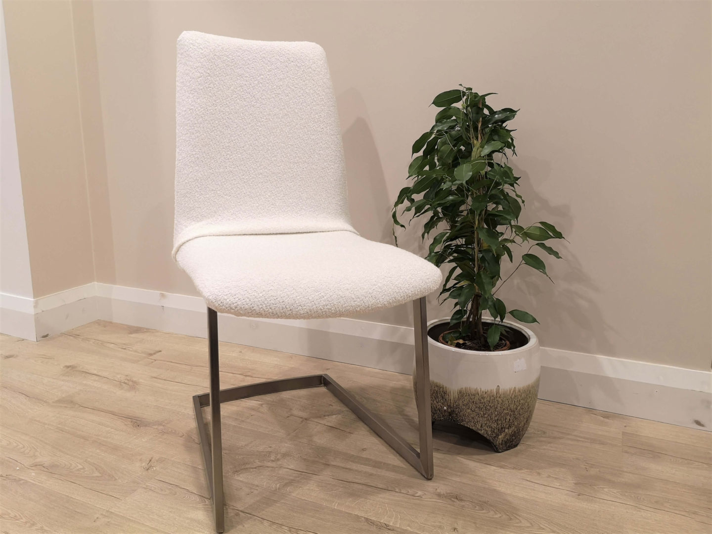 A dining chair with a white boucle material chair cover sitting next to a green plant.