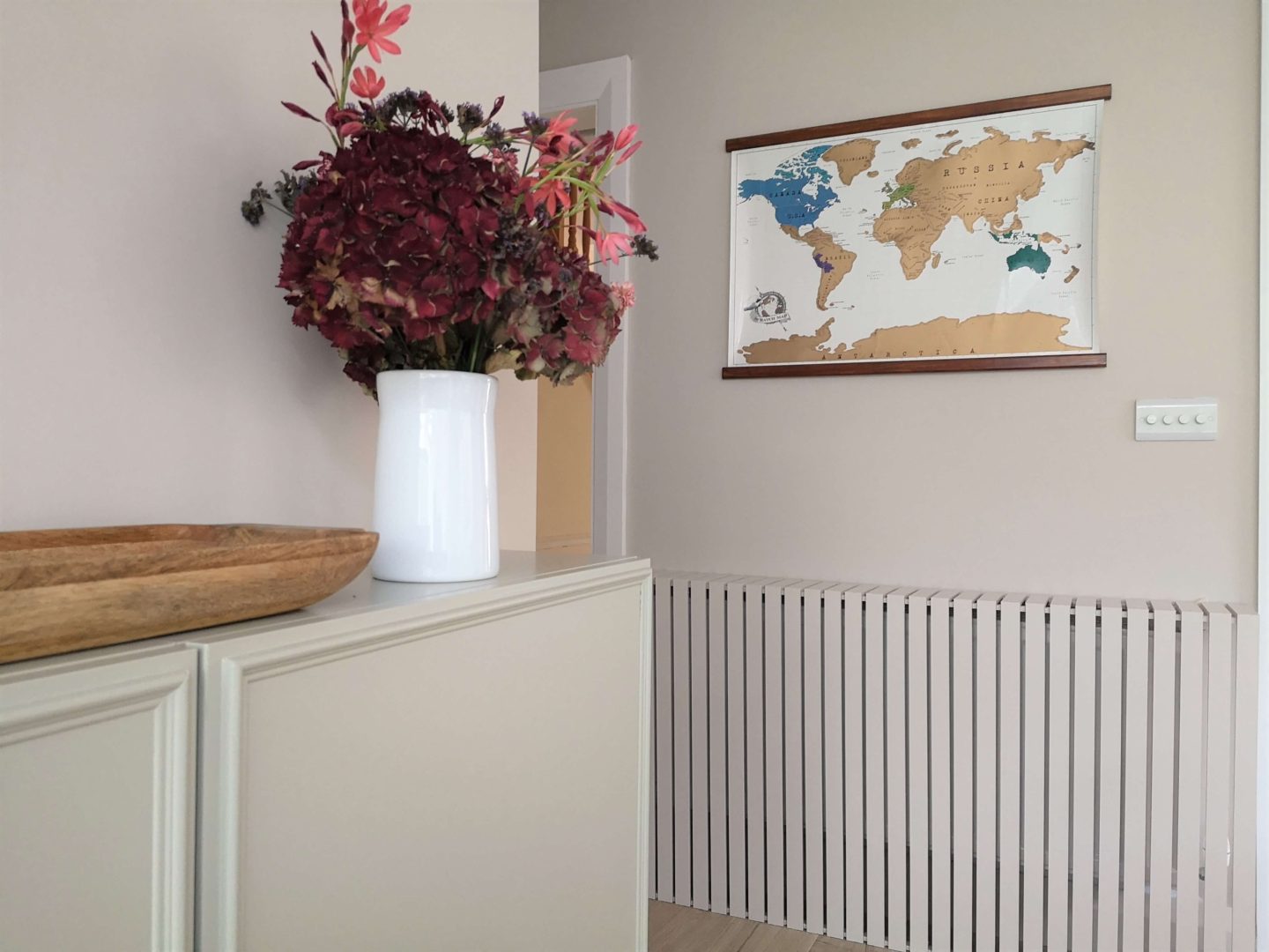 A world map hanging on the wall with wooden slats as the frame. Underneath is radiator cover made using slats.