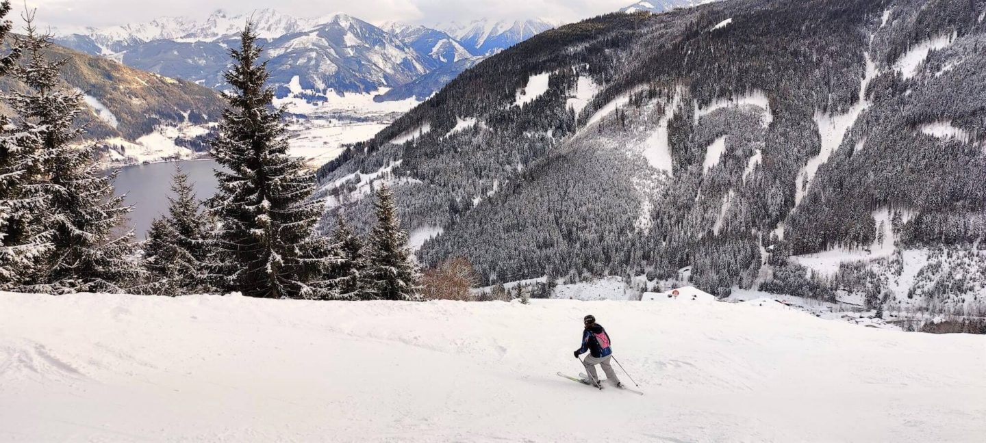 A woman skiing down a slope with the lake of Zell am See in the background.