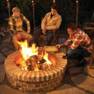 Several people seated around a brick firepit.