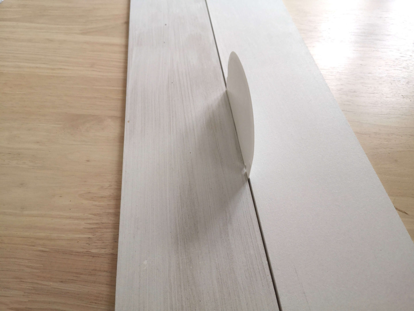Two boards of MDF, laying on a table, with a dough scraper as a spacer between them.