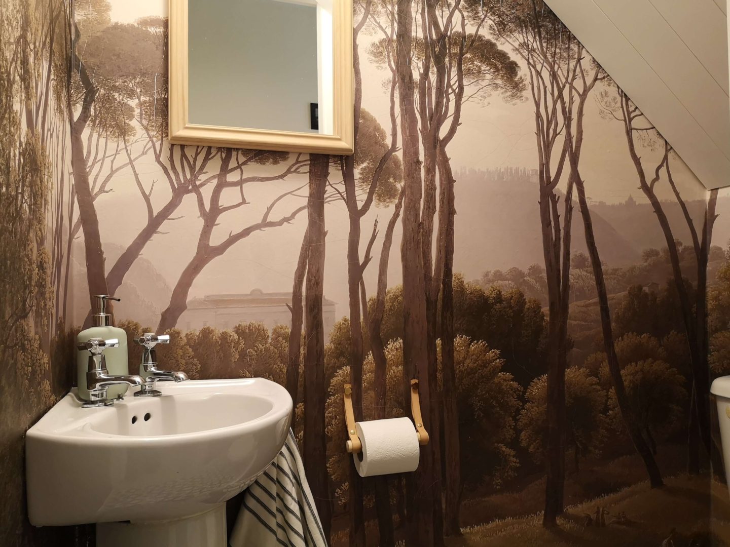 A tiny bathroom with a wallpaper mural on all four walls, a shiplap ceiling and black and white geometric tiles.