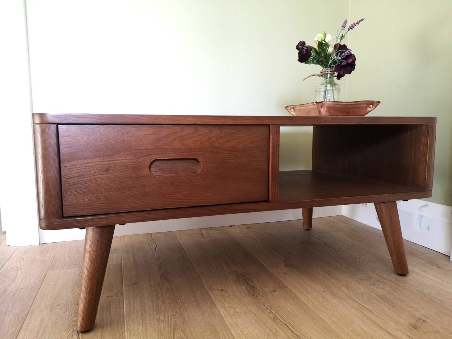 A walnut coffee table in front of a freshly painted green wall. 