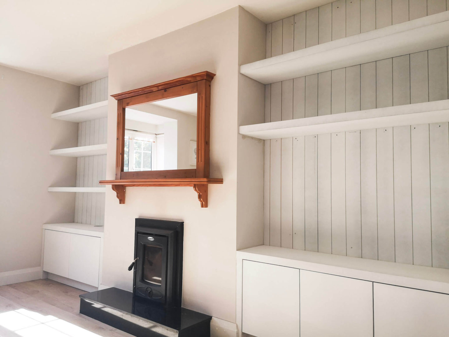 A living room built in with primed shiplap on either side of the fireplace, with chunky shelves and storage on the bottom with plain flat doors.
