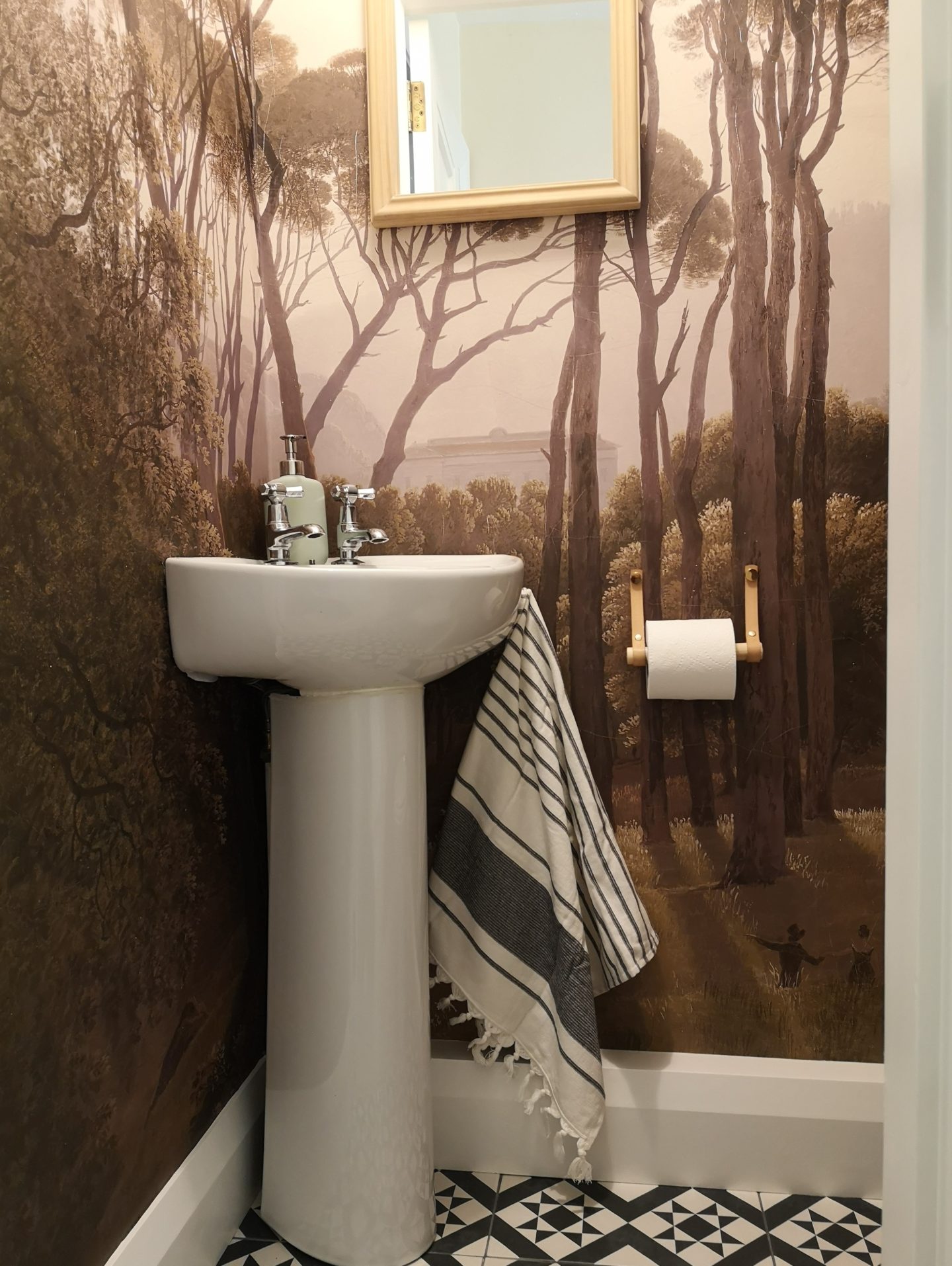 A bathroom under the stairs with a forest mural on the walls.