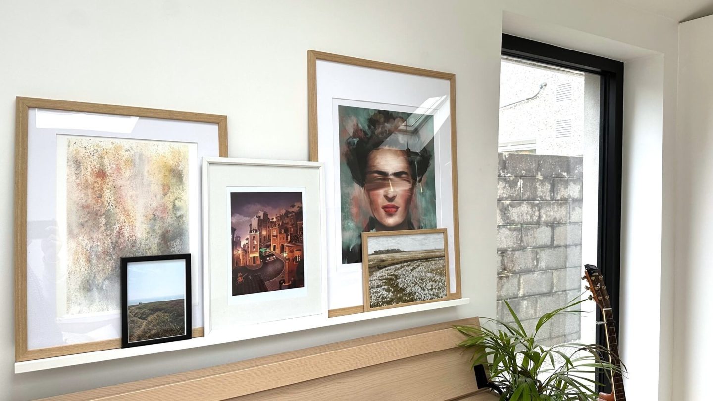 A gallery wall with digital prints as some of the artwork. Framed pictures are sitting on a picture ledge above a piano.