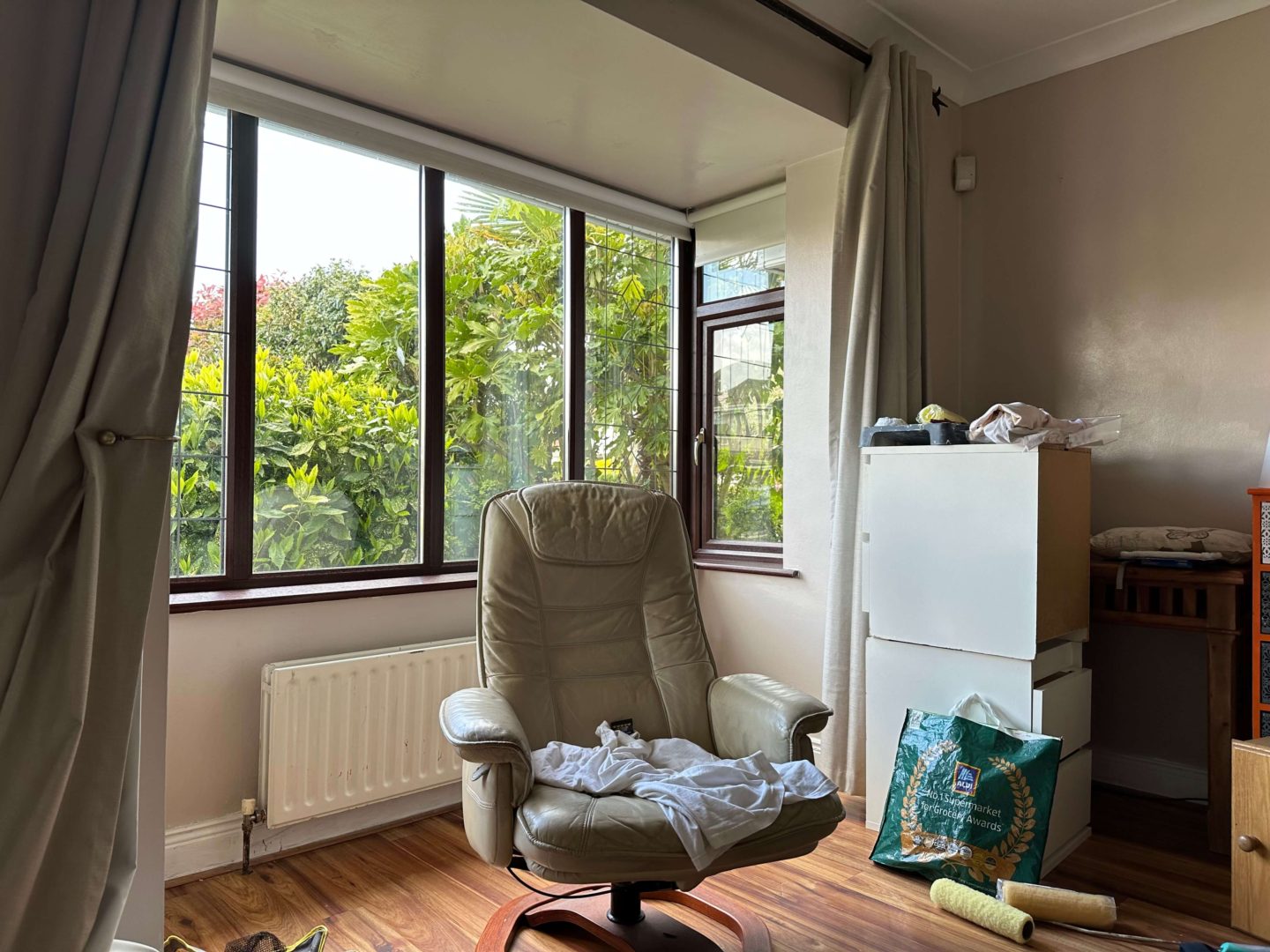 A before picture of a living room with dark taupe walls. A bay window in the room is also shown.