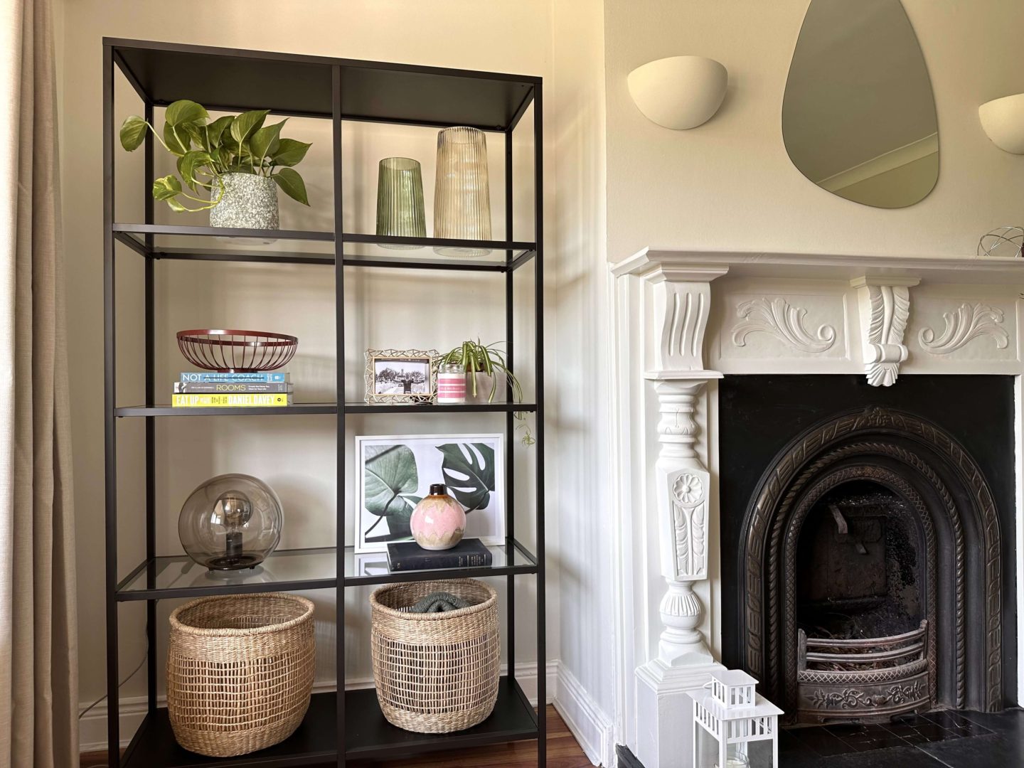 A black shelving unit next to a white fireplace.