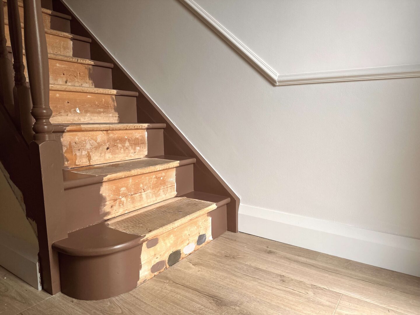 A hallway renovation showing a newly painted brown stairs, ready for a runner. The wall has a dado rail. Above the dado rail is painted white and below the dado rail is painted a warm, light greige.