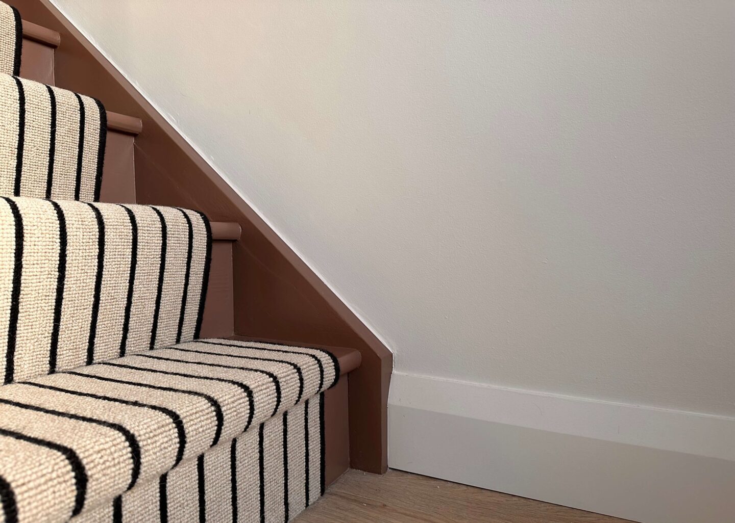 A black and cream striped carpet on a reddish-brown painted stairs.